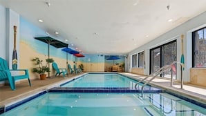 An indoor swimming pool with clear blue water, surrounded by turquoise chairs and umbrellas, and a mural of a beach scene on the walls. - 4 Bedroom Condo at Gateway Lodge Near Mountain House Base (Keystone)