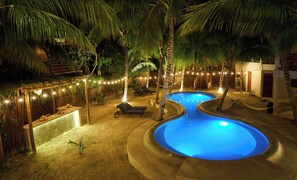 A nighttime outdoor pool area with two pools, lounge chairs, and string lights. - Casa del Viento by ÓOL Hotels (Isla Holbox)
