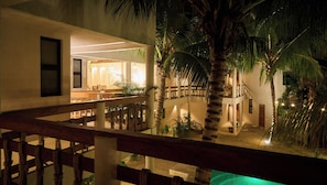 A multi-level building with a balcony, palm trees, and a well-lit interior.