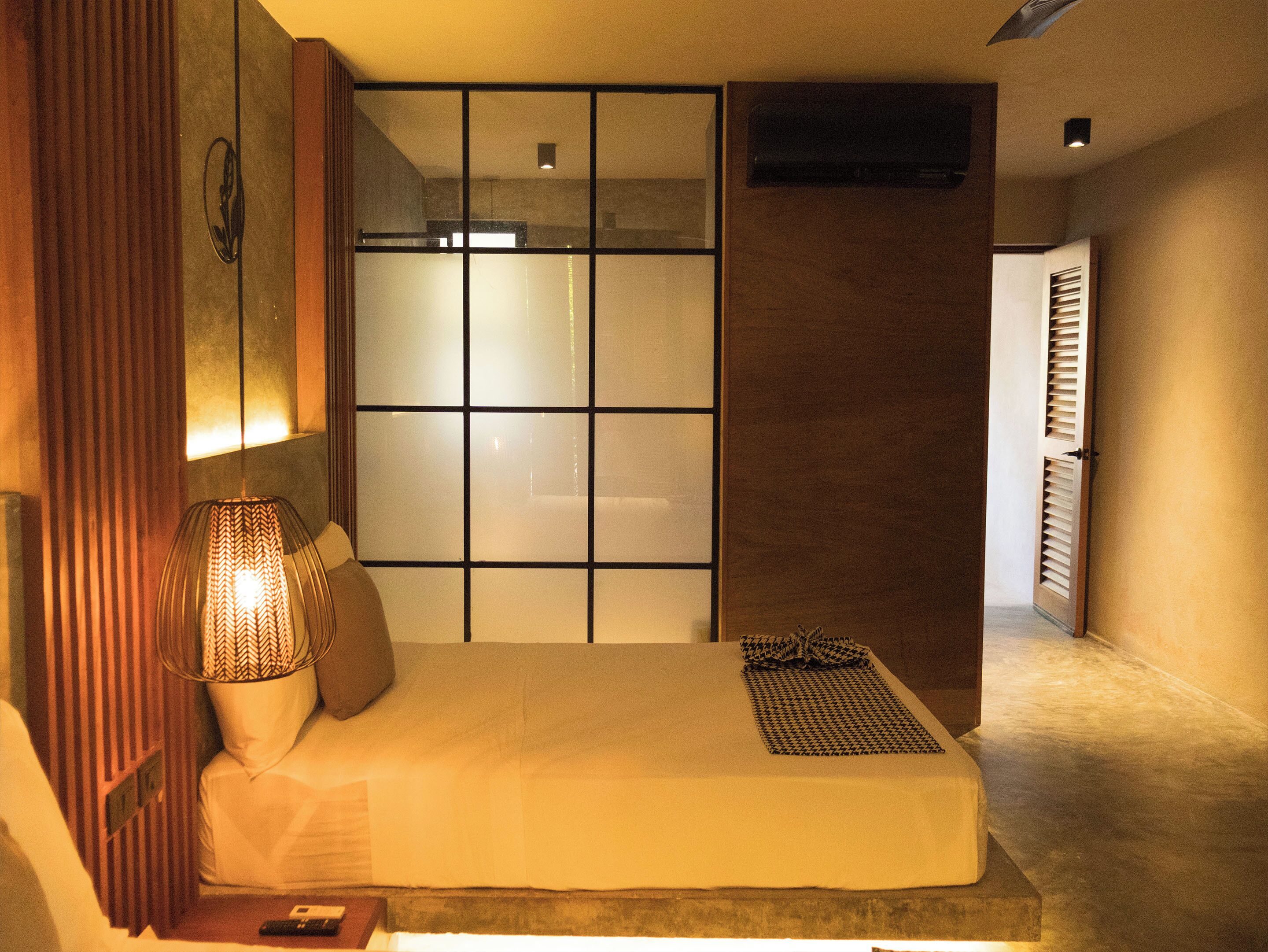 A bedroom with a bed, a bedside lamp, a window with blinds, and a door.