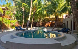 A circular pool with lounge chairs, surrounded by palm trees and a thatched roof structure.