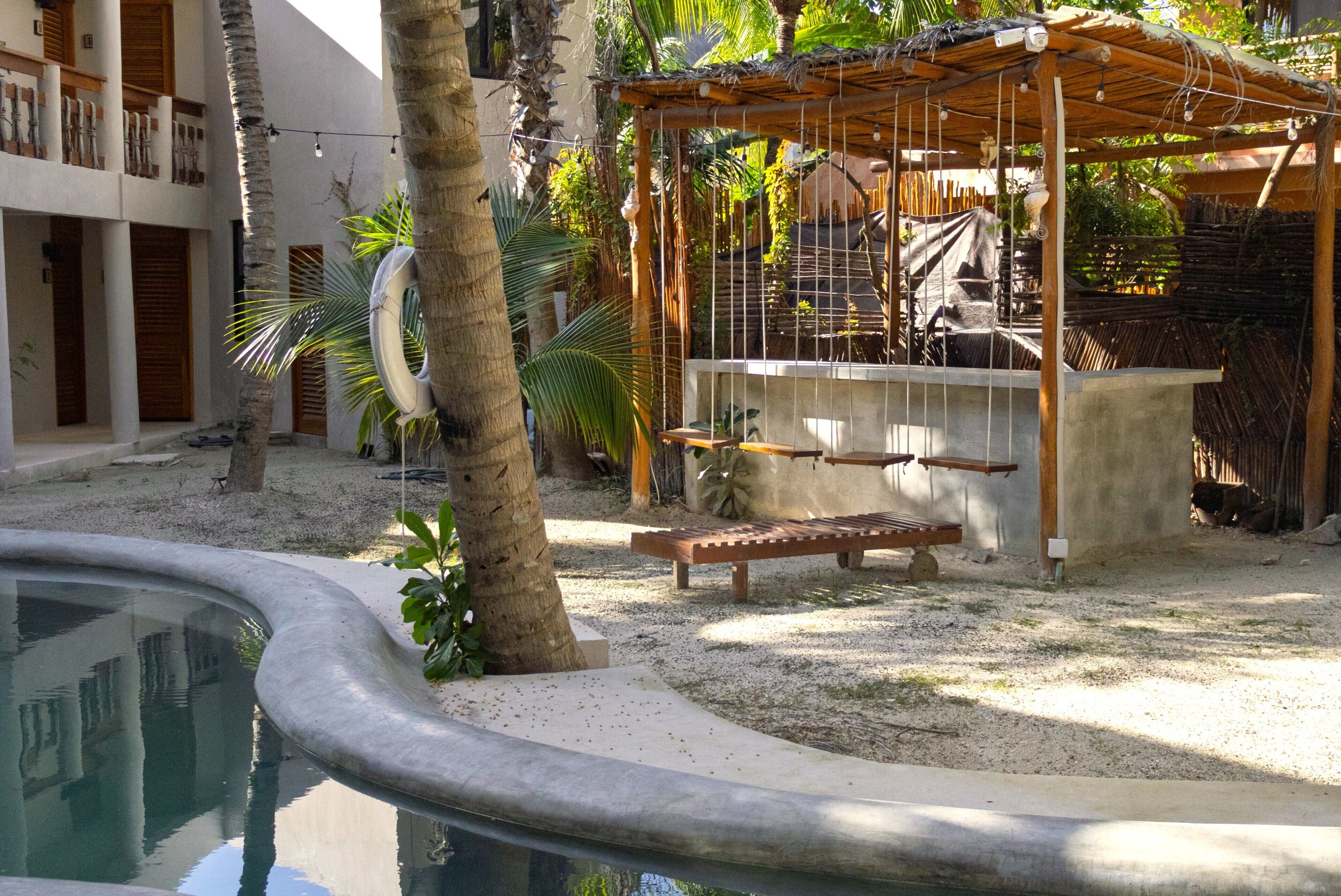 A pool area with a wooden bench, a shaded seating area, and a building with multiple balconies.