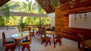 Un comedor interior con mobiliario de madera, ventanas amplias y plantas colgantes.