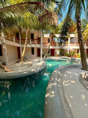Un'area piscina con palme, una vasca idromassaggio e un edificio con balconi.