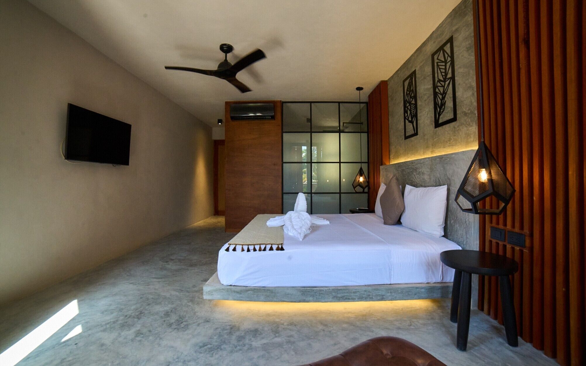 A hotel room with a bed, a ceiling fan, a flat-screen TV, and a wall-mounted air conditioning unit.