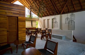 Um espaço amplo e interno, com móveis de madeira, telhado de palha e gaiolas de pássaros penduradas.