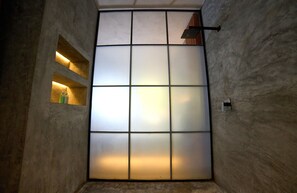 A room with a large frosted glass partition, a small shelf with toiletries, and a hanging light fixture.