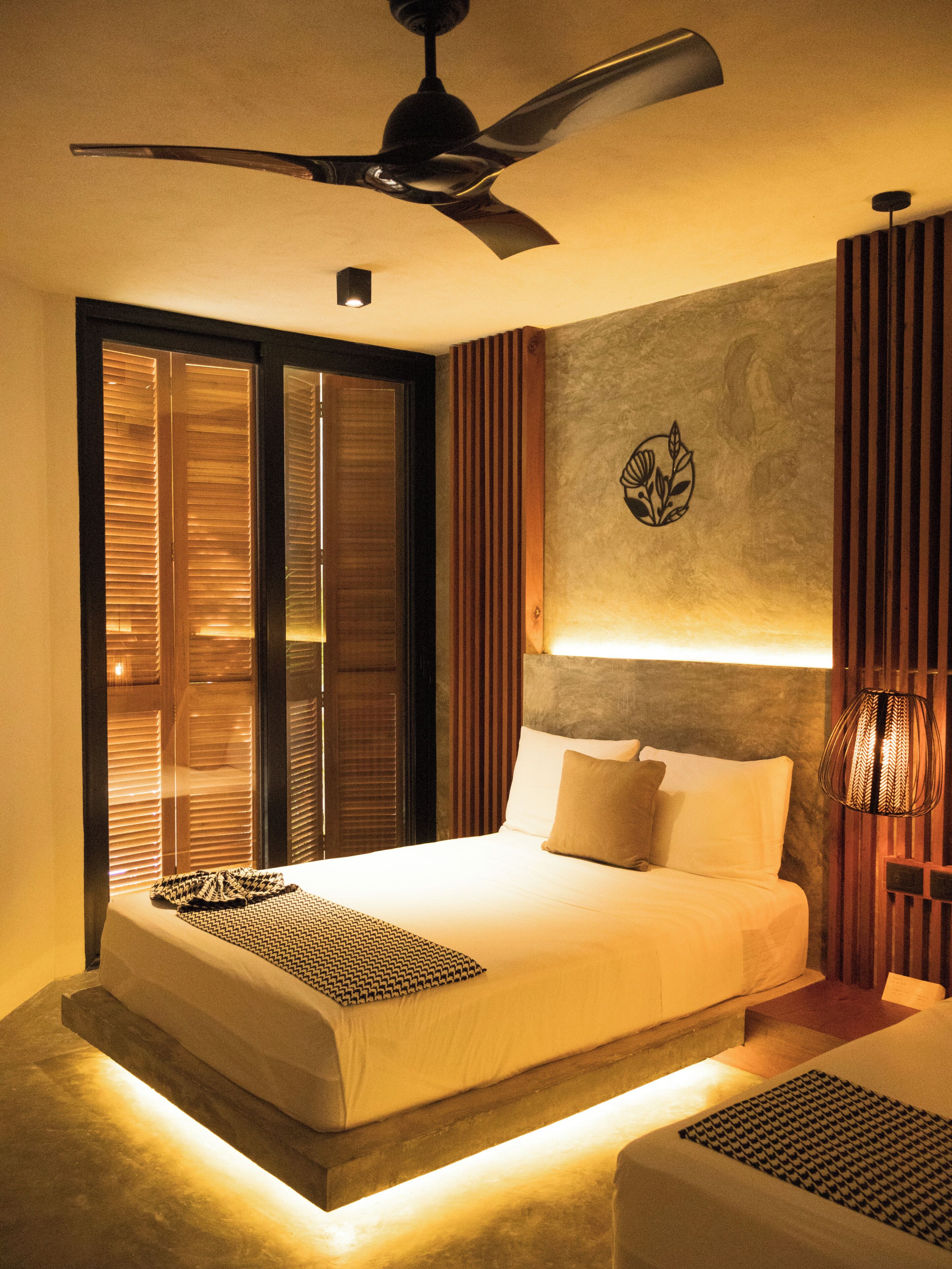 Une chambre à coucher moderne, avec un lit, un ventilateur de plafond, une lampe fixée au mur et un élément décoratif mural.