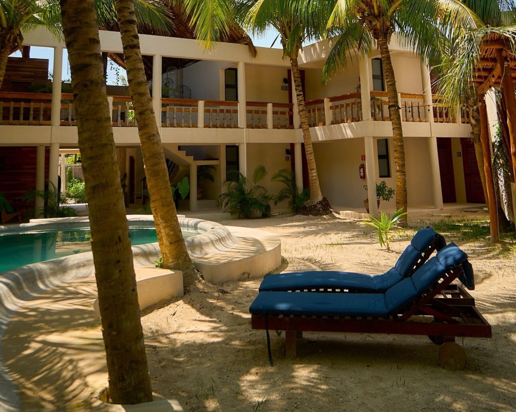 A resort with a pool, lounge chairs, palm trees, and a multi-story building.
