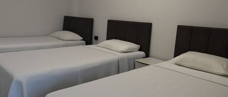 Habitación de hotel con tres camas individuales, cada una con cabecera y mesita de noche.