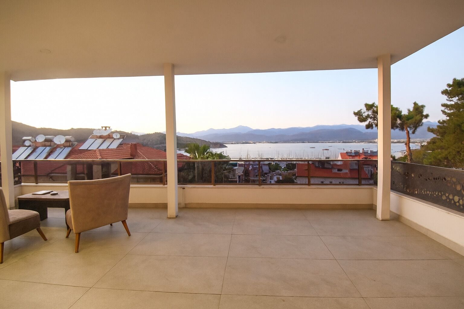 Un balcone con vista su un lago e montagne, un tavolo con sedie e pannelli solari sul tetto.