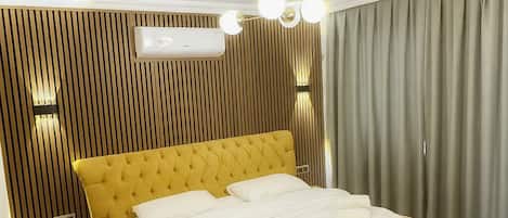 A modern hotel room with a large bed, wooden paneling on the walls, a ceiling vent, and a window with curtains.