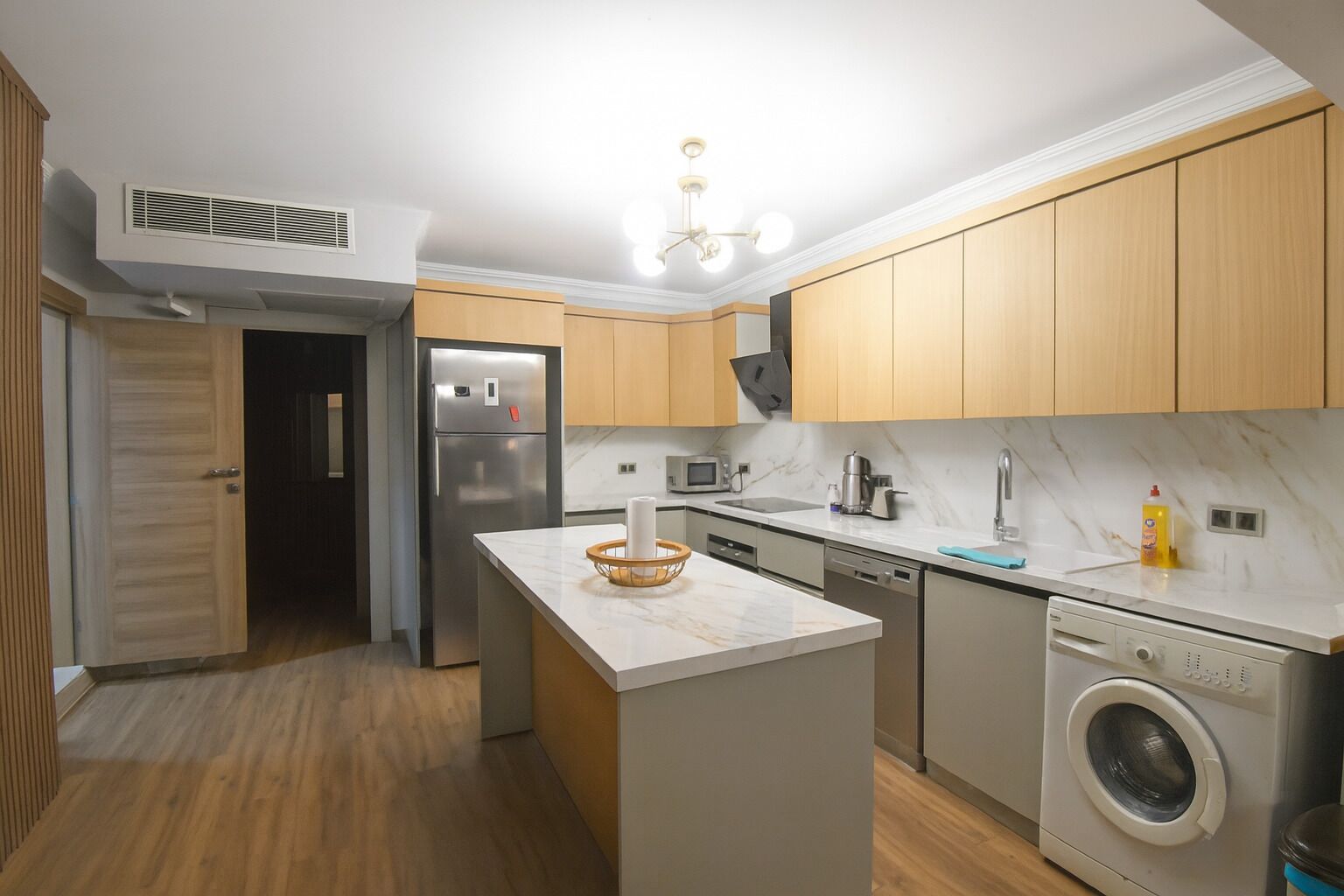 Eine moderne Küche mit Holzschränken, einem Edelstahlkühlschrank, einer eingebauten Waschmaschine und einer Marmorarbeitsplatte.