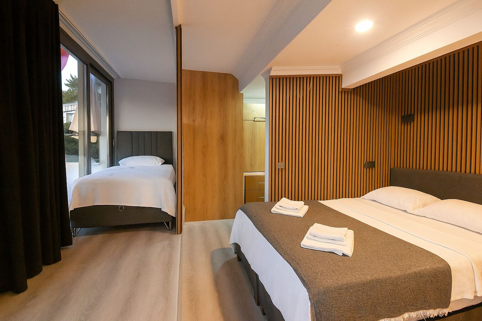 A hotel room with two beds, a large window, and a wooden accent wall.