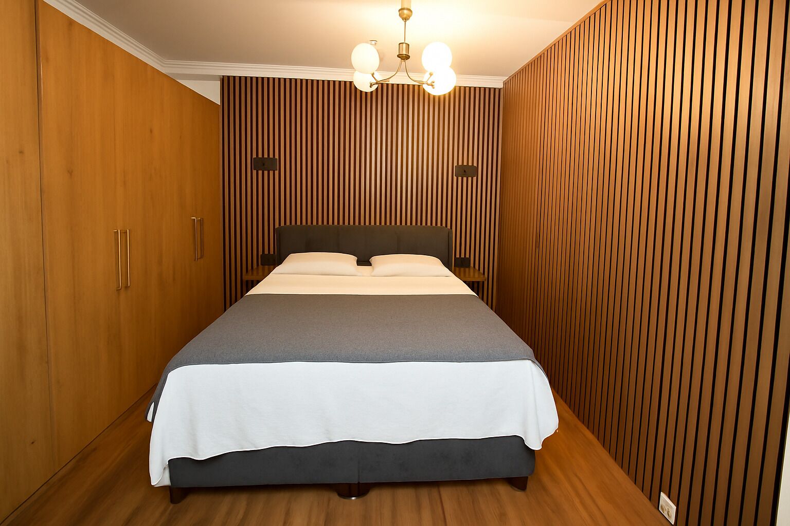 A bedroom with a bed, wooden wardrobe, and a wall-mounted light fixture.