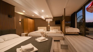 A modern hotel room with a large bed, two smaller beds, a TV, and a balcony with a view.
