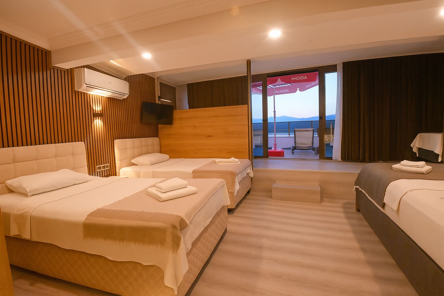 Quarto de hotel com três camas, uma televisão, ar condicionado e varanda com vista.