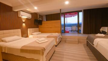 Quarto de hotel com três camas, uma televisão, ar condicionado e varanda com vista.