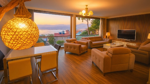 A modern living room with a view of the city and mountains, a dining area with a table and chairs, and a large TV on the wall.