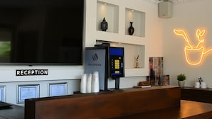 A reception area with a modern design, including a reception desk, a digital kiosk, and a neon plant sign.