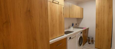 A compact kitchen with wooden cabinets, a washing machine, and a small trash bin.