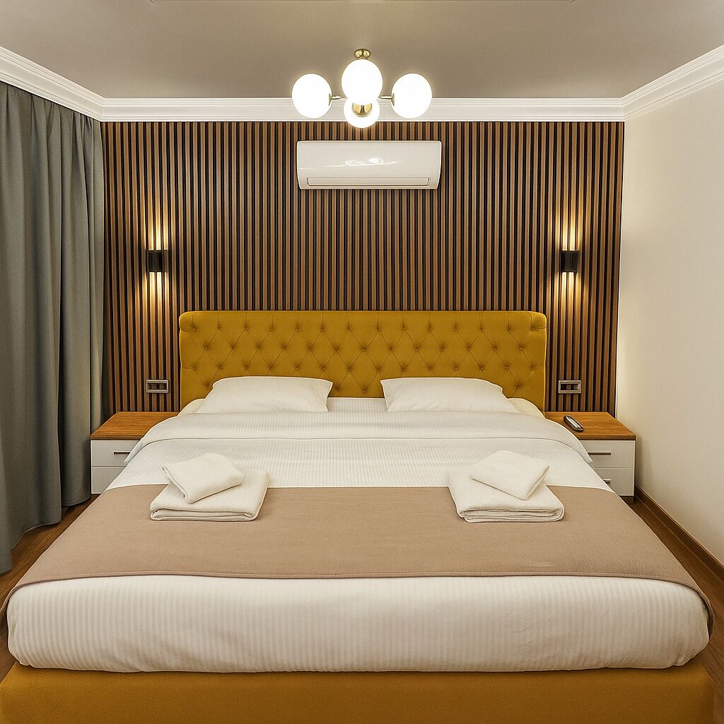 A hotel room with a large bed, a tufted headboard, bedside lamps, and a ceiling-mounted air conditioning unit.