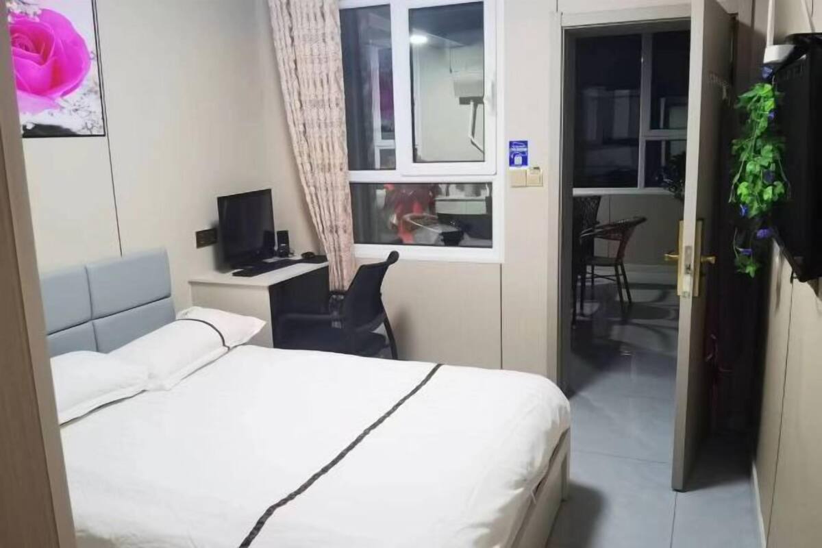 Ein Hotelzimmer mit einem Bett, einem Schreibtisch mit Computer, einem Stuhl, einem Fenster mit Blick und einer Tür zu einem anderen Raum.