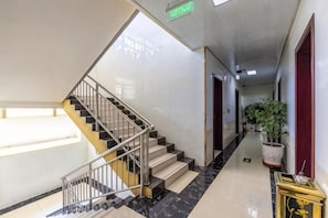 A hotel corridor with a staircase, a potted plant, and a framed picture on a console table. - Yuzhong Senshu Business Hotel (Yuzhong)