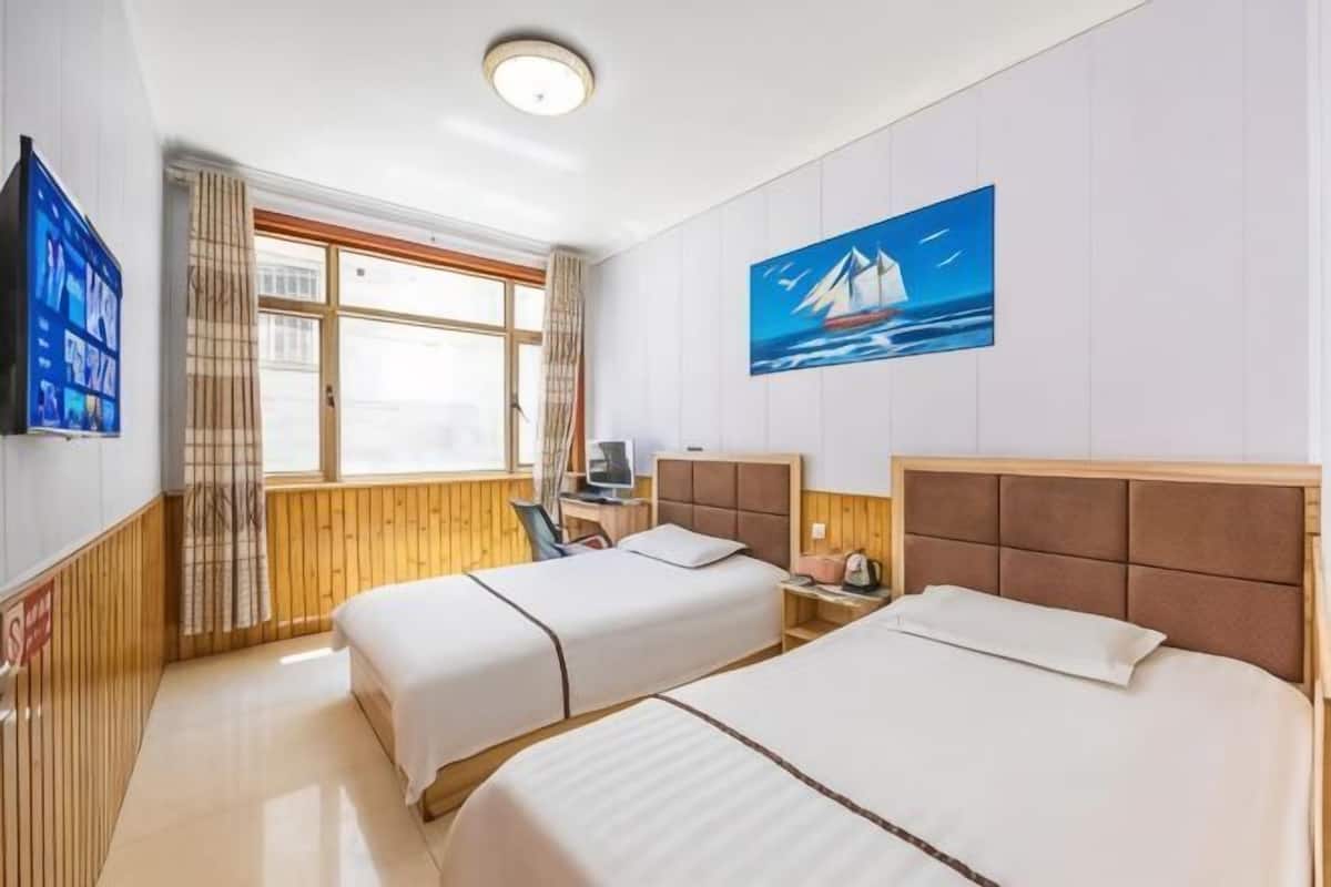 Ein Hotelzimmer mit zwei Betten, einem Fernseher, einem Segelbootgemälde und einem fenster mit Vorhängen.
