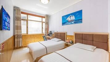 A hotel room with two beds, a television, a painting of a sailboat, and a window with curtains.