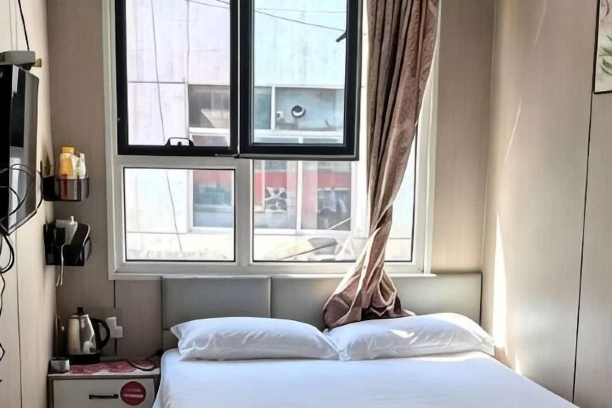 Ein Hotelzimmer mit Bett, Fenster mit Vorhängen, Nachttisch mit Lampe und einem an der Wand befestigten Telefon.