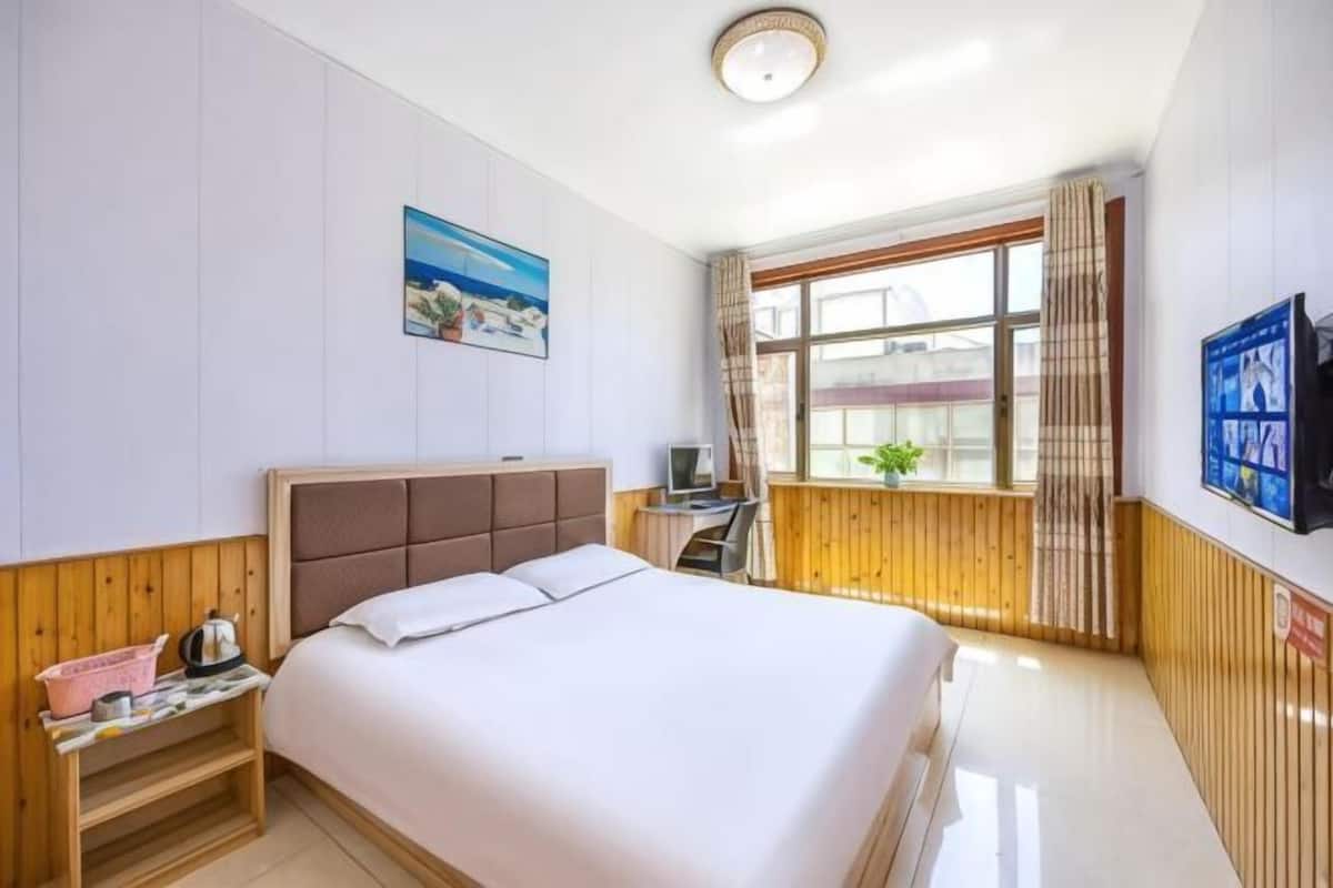 Ein Hotelzimmer mit Bett, Schreibtisch, Fernseher, einem Fenster mit Vorhängen und einem Bild an der Wand.