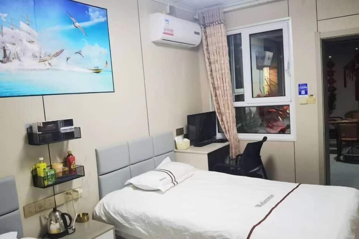 Ein Hotelzimmer mit einem Bett, einem Fernseher, einem Schreibtisch mit Computer, einem Fenster mit Vorhängen und einer Wand-Klimaanlage.