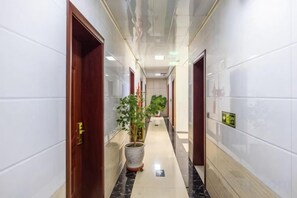 Een hotelgang met deuren, een kamerplant en betegelde muren.