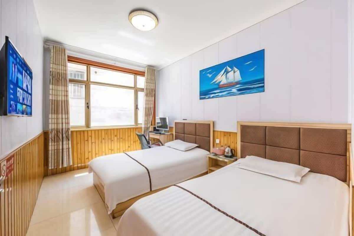 Ein Hotelzimmer mit zwei Betten, einem Schreibtisch, einem Sessel, einem Fernseher und einem Fenster mit Vorhängen.