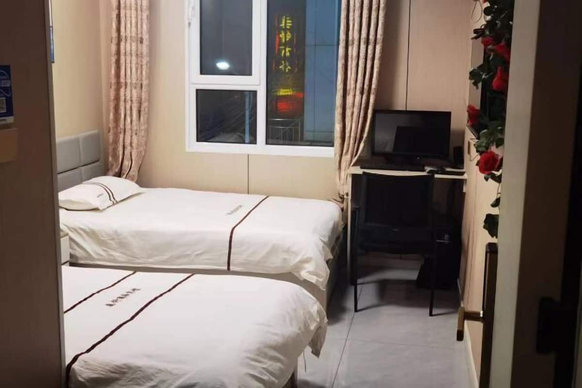 Ein Zimmer mit zwei Betten, einem Schreibtisch mit Computer und einem Fenster mit Vorhängen.