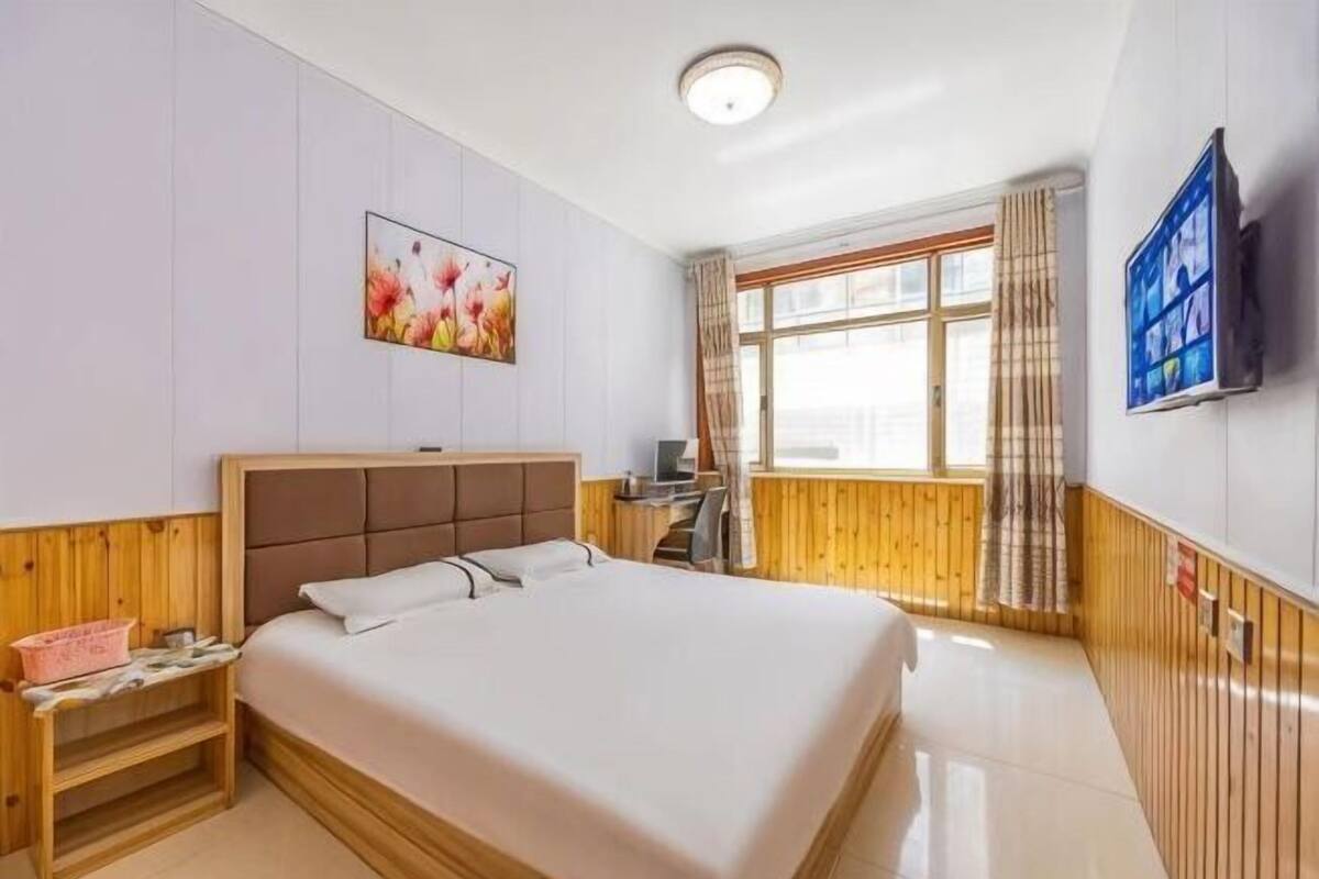 Ein Hotelzimmer mit Bett, Schreibtisch, Stuhl, Fernseher und einem Fenster mit Vorhängen.