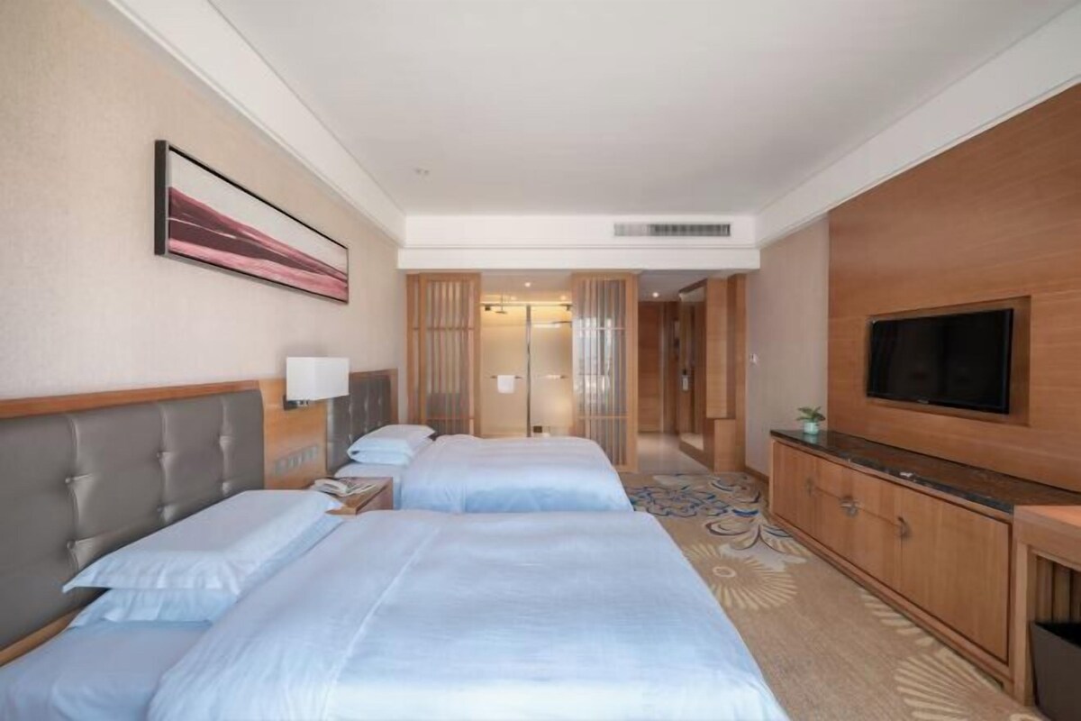 A hotel room with two beds, a TV, a cabinet, and a painting on the wall.