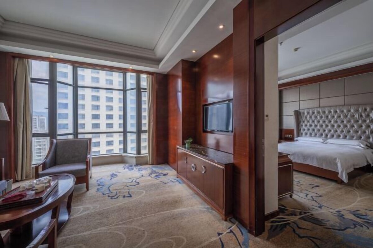 A hotel room with a large window, a television, a bed, a desk, and a chair.