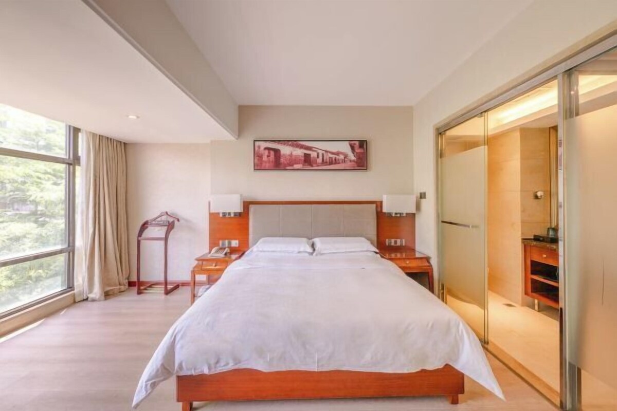A modern hotel room with a large bed, a nightstand, a bedside table, a wardrobe, and a window with curtains.