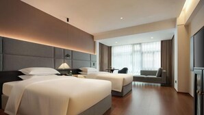 Une chambre d’hôtel moderne avec deux lits, un canapé, un bureau et une grande fenêtre.