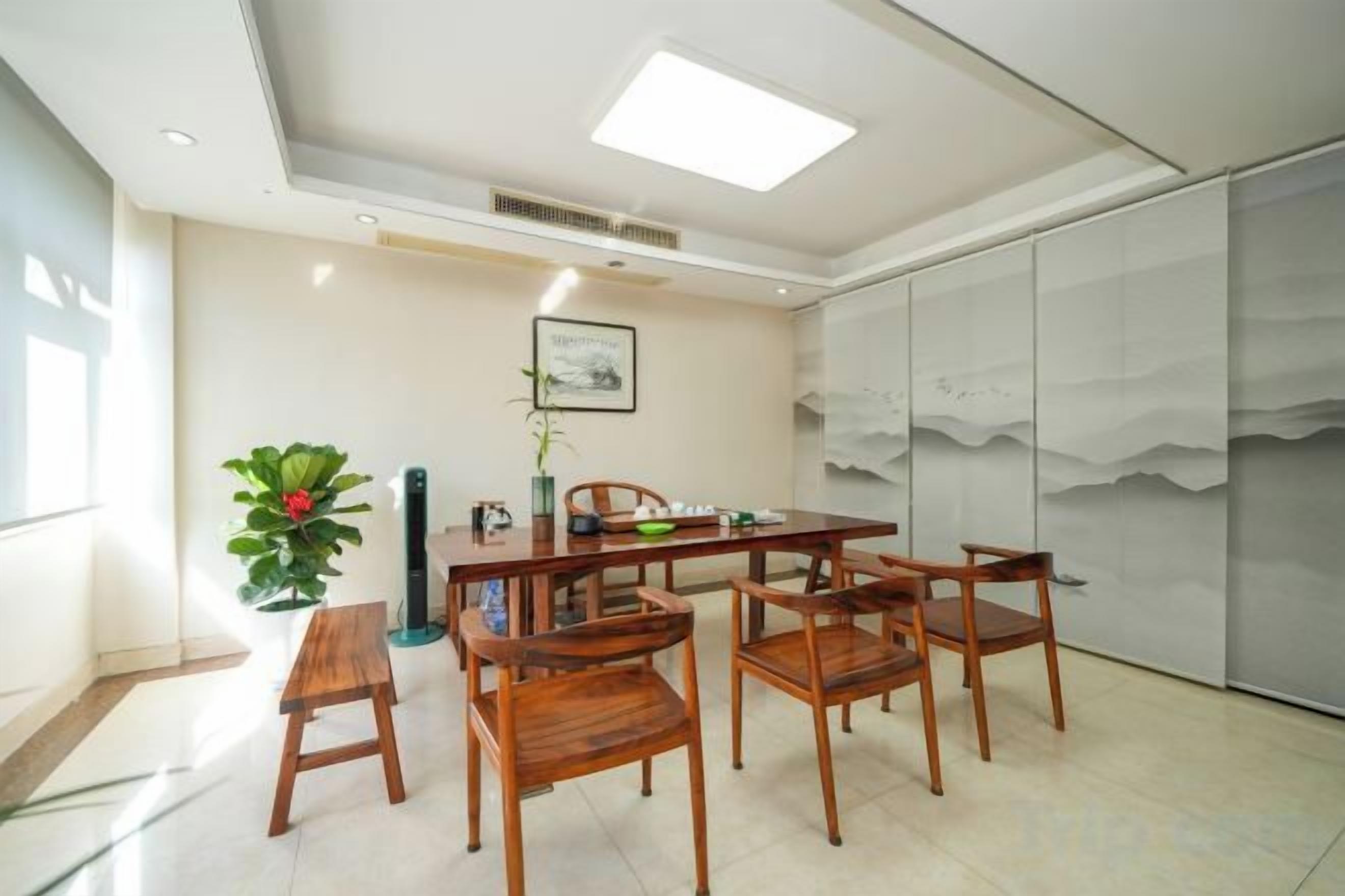 A dining area with a table and chairs, a potted plant, and a wall with a mountain painting.
