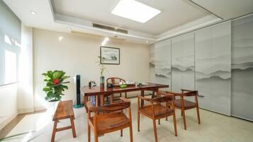 A dining area with a table and chairs, a potted plant, and a wall with a mountain painting.