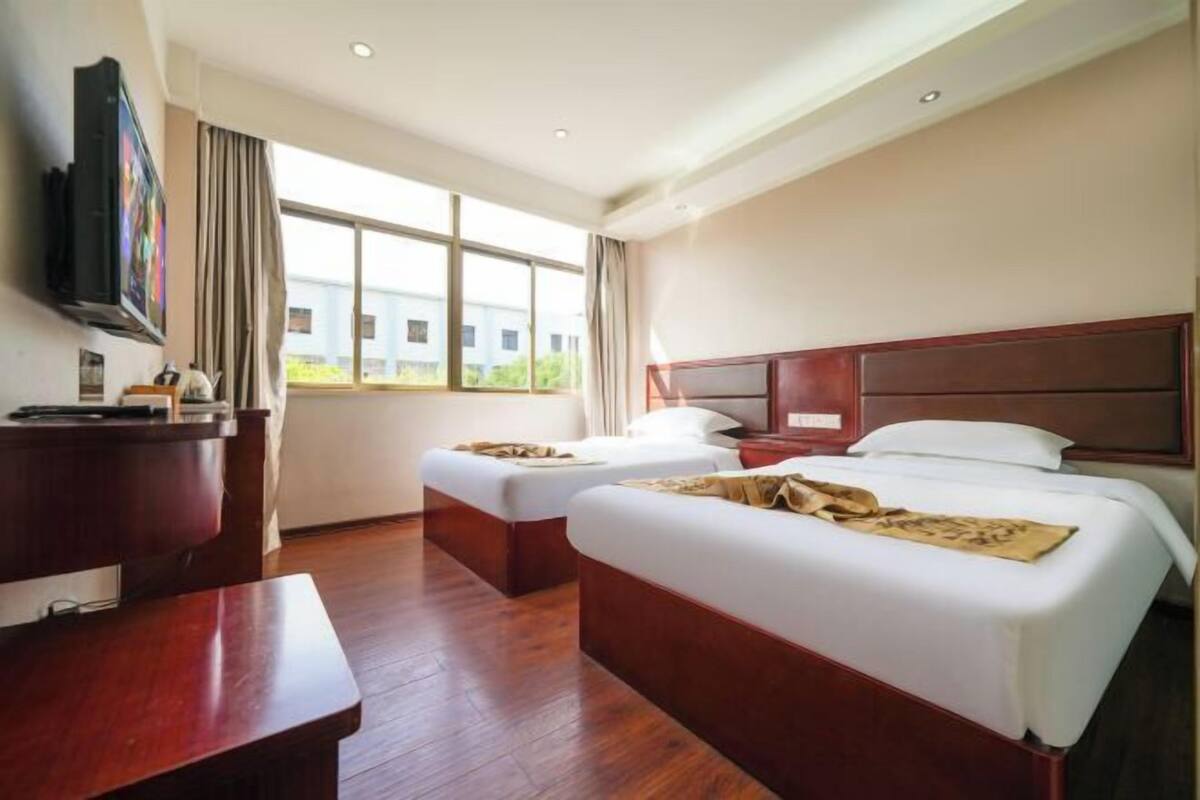 A hotel room with two beds, a desk, a TV, and large windows.