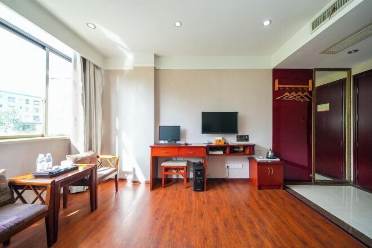 A hotel room with a wooden floor, a desk with a computer, a TV, a bed, and a wardrobe.