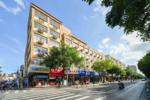 Un edificio de varios pisos con comercios en la planta baja, un paso de peatones y una calle arbolada.