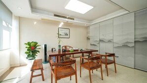 A dining area with a wooden table and chairs, a small wooden stool, a potted plant, and a framed picture on the wall. - Changtai Hezheng Business Hotel (Zhangzhou)