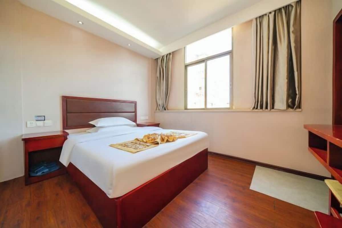 A hotel room with a wooden bed, a nightstand, a window with curtains, and a built-in shelf.
