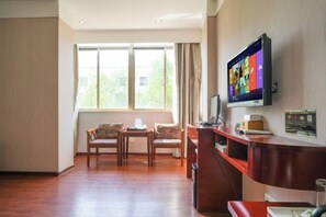 A hotel room with a wooden floor, a desk with a computer, a television mounted on the wall, and a window with curtains. - Changtai Hezheng Business Hotel (Zhangzhou)