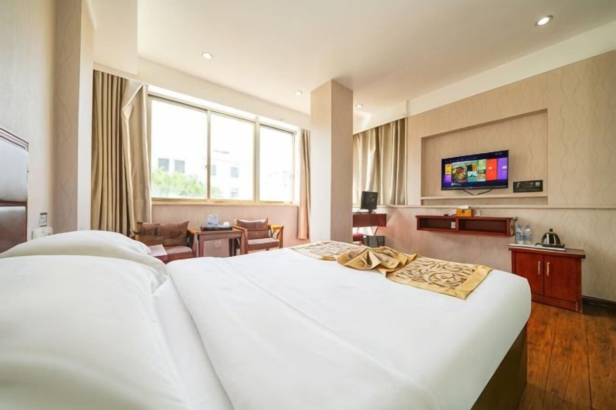 A hotel room with a large bed, a desk, a television, and a window with curtains.